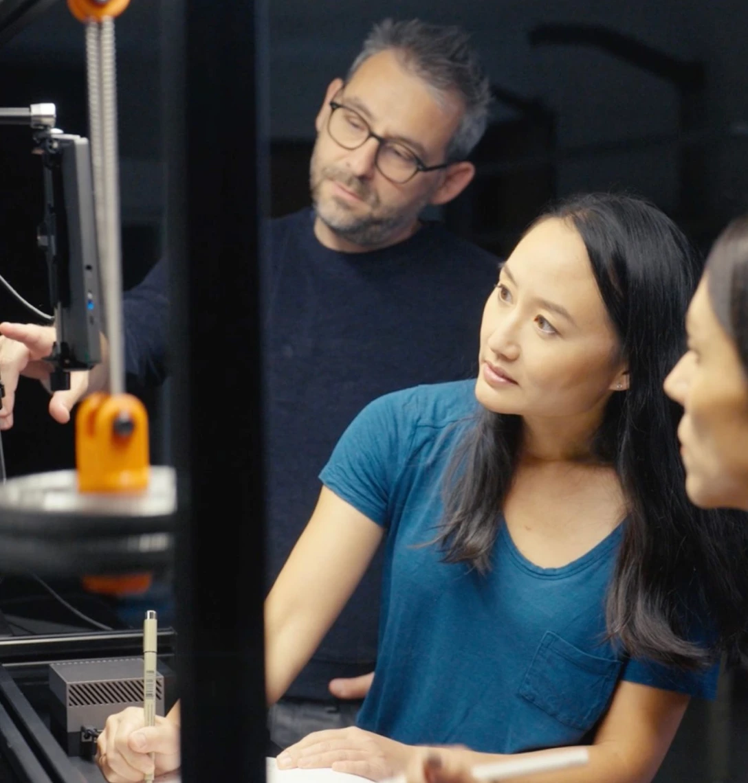 Three people reviewing work at a machine